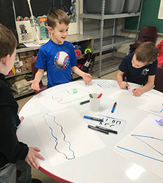 Three boys at a round table drawing with colored markers
